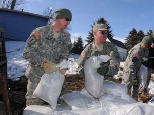 Spc. Tim Sybrant, of the 817th Engineer Sapper Company (Jamestown, N.D.), left, passes sandbags to Pfc. Scott Ness, of the 188th Engineer Company (Wahpeton, N.D.), March 17, in the Backyard of Konny Zinns and her husband Sgt. Darin Zins, who is currently deployed to Kosovo and can do little more than empathize with his family during Skype calls from half a World away. He serves with the 231st Maneuver Task Force, part of the NATO peacekeeping forces in Kosovo Force 12. The soldiers are building a sandbag flood barrier to hold back rising water from the Sheyenne River. (DoD photo by Senior Master Sgt. David H. Lipp) (Released)