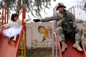 Sgt. Stephen Covell, a native of Pacific Grove, Calif., along with an Iraqi girl go down a slide at the playground during the reopening of the Al-Moutasam Kindergarten March 3 in the Rusafa district of eastern Baghdad. Covell is a medic assigned to Headquarters and Headquarters Troop, 5th Squadron, 73rd Cavalry Regiment, 3rd Brigade Combat Team, 82nd Airborne Division, Multi-National Division-Baghdad