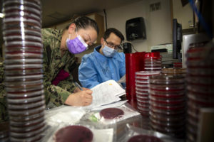 NEW YORK (April 21, 2020) Lt. Cmdr. Tida Lee, left, confers with Hospital Corpsman 3rd Class Jeremy Parr regarding a patient's cultured results in the microbiology lab aboard the hospital ship USNS Comfort (T-AH 20). Comfort cares for critical and non critical patients without regard to their COVID-19 status. Comfort is working with Javits New York Medical Station as an integrated system to relieve the New York City medical system, in support of U.S. Northern Command's Defense Support of Civil Authorities as a response to the COVID-19 pandemic. (U.S. Navy photo by Mass Communication Specialist 2nd Class Sara Eshleman/Released)200421-N-EV253-1011