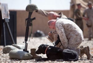 Yeager, an improvised explosive device detection dog, lies in front of a battlefield cross as Staff Sgt. Derick Clark, a kennel supervisor with Headquarters and Service Company, 2nd Battalion, 9th Marine Regiment, and 26-year-old native of Hillsdale, Mich., and Chief Warrant Officer 2 Michael Dale Reeves, a kennel officer in charge with 2nd Bn., 9th Marines and 41-year-old native of Mt. Pleasant, S.C., observe a moment of silence in honor of Lance Cpl. Abraham Tarwoe, a dog handler and mortarman who served with Weapons Company, 2nd Bn., 9th Marines, during a memorial service here, April 22, 2012. Tarwoe, who became Yeager's handler in July 2011, was killed in action during a dismounted patrol in support of combat operations in Helmand province's Marjah district, April 12. Tarwoe's fellow Marines remember him for his contagious laughter and smile, and his unfaltering courage on the battlefield. (U.S. Marine Corps photo by Cpl. Alfred V. Lopez)